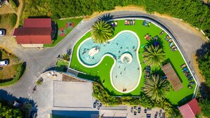 Vista aérea de un resort con una piscina grande, palmeras y un edificio de techo rojo.