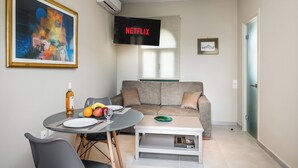 A modern living room with a gray sofa, a round dining table with a bottle and fruit, a framed painting, and a mounted TV displaying "NETFLIX". - Villa Liostasi (Corfu)