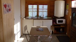 Een kleine keuken met houten wanden, een raam met hartvormige decoraties, een spoelbak, een magnetron en een tafel met stoelen.