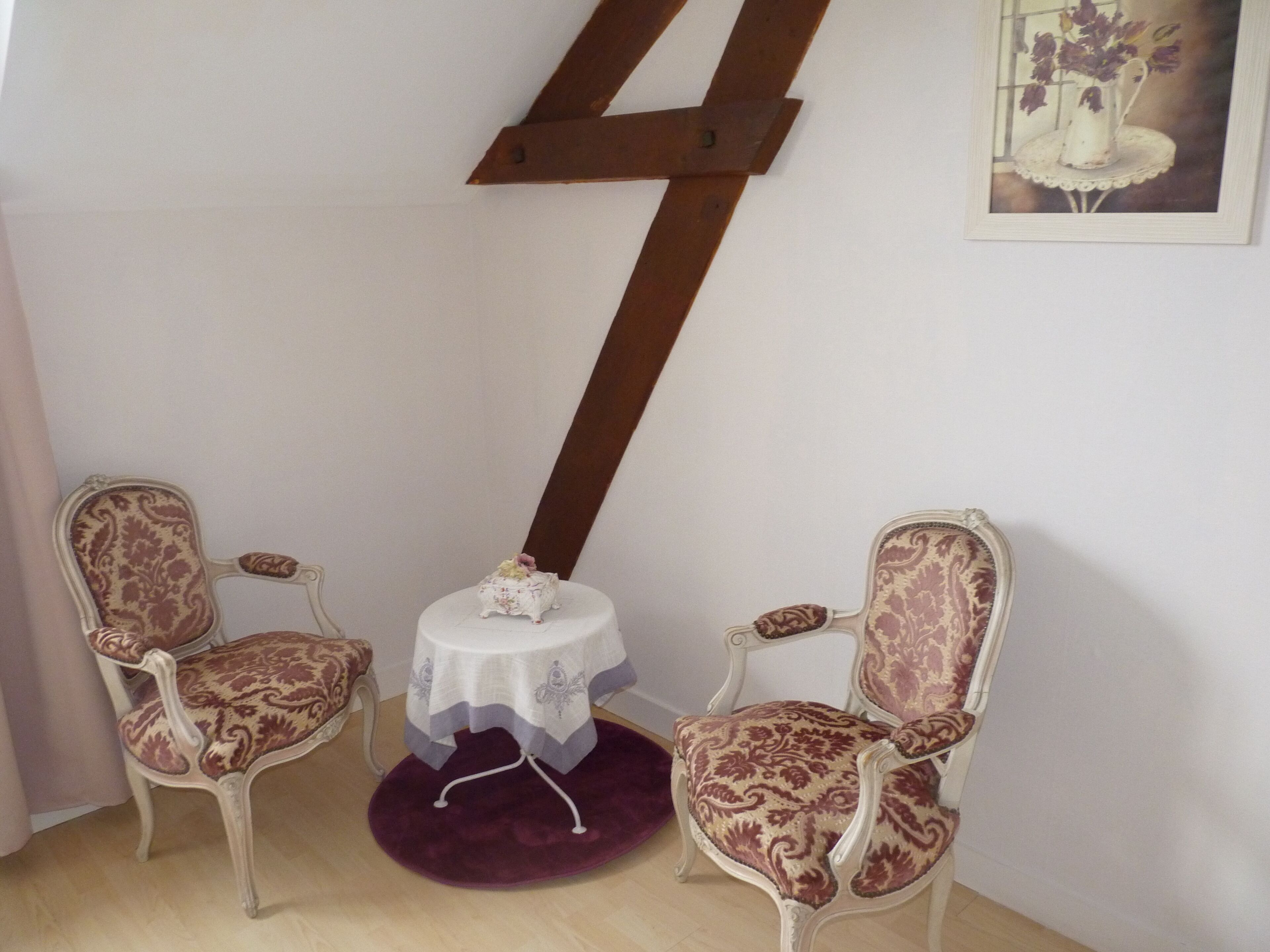 Une pièce comprenant deux fauteuils richement décorés, une petite table ronde recouverte d’une nappe blanche et un élément décoratif mural.