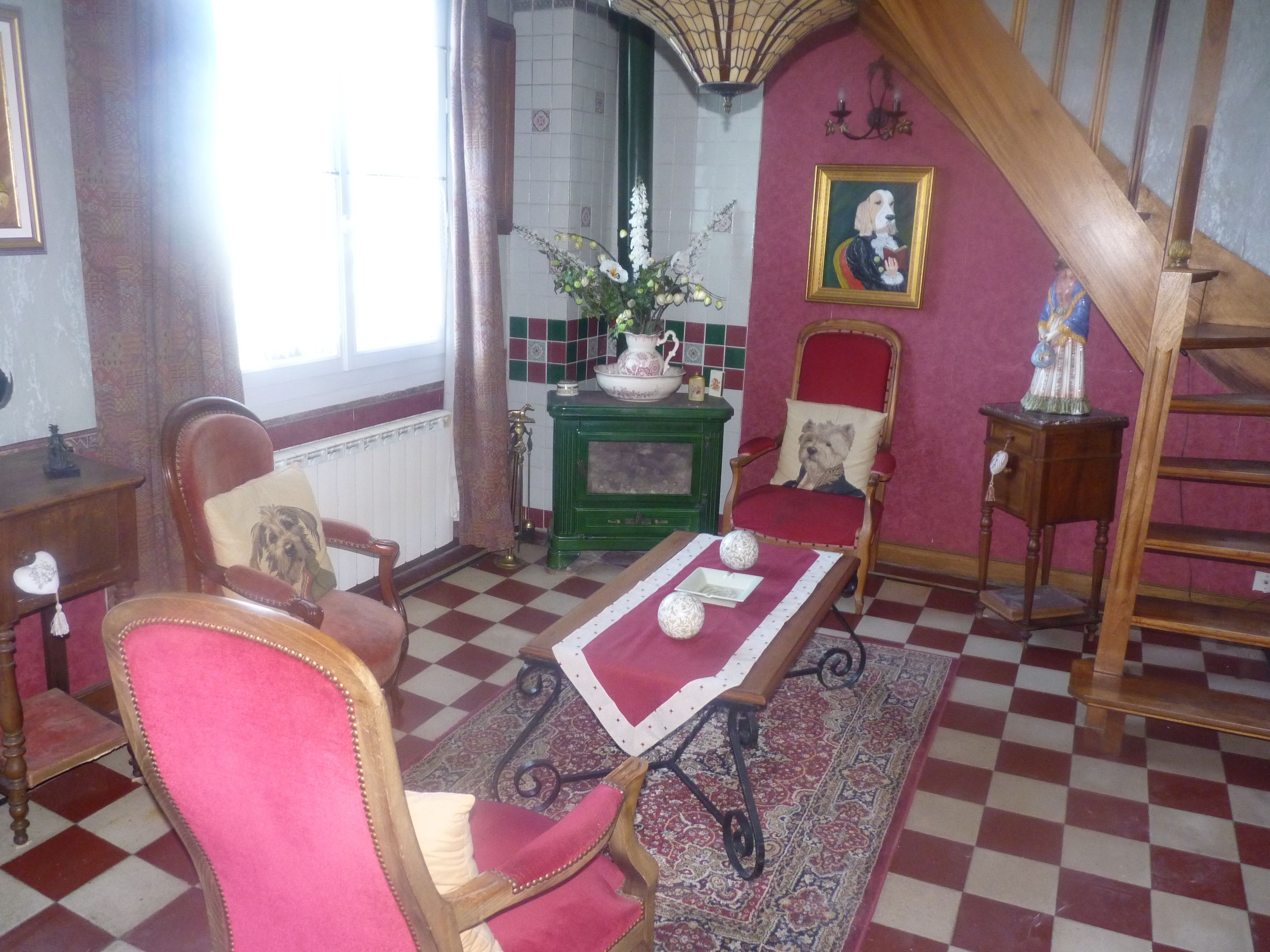 Une pièce au décor traditionnel, avec un sol à carreaux, une cheminée verte, un fauteuil rouge et un escalier en bois.