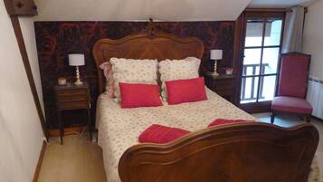 A bedroom with a wooden bed, two bedside tables with lamps, a chair, and a window with curtains.