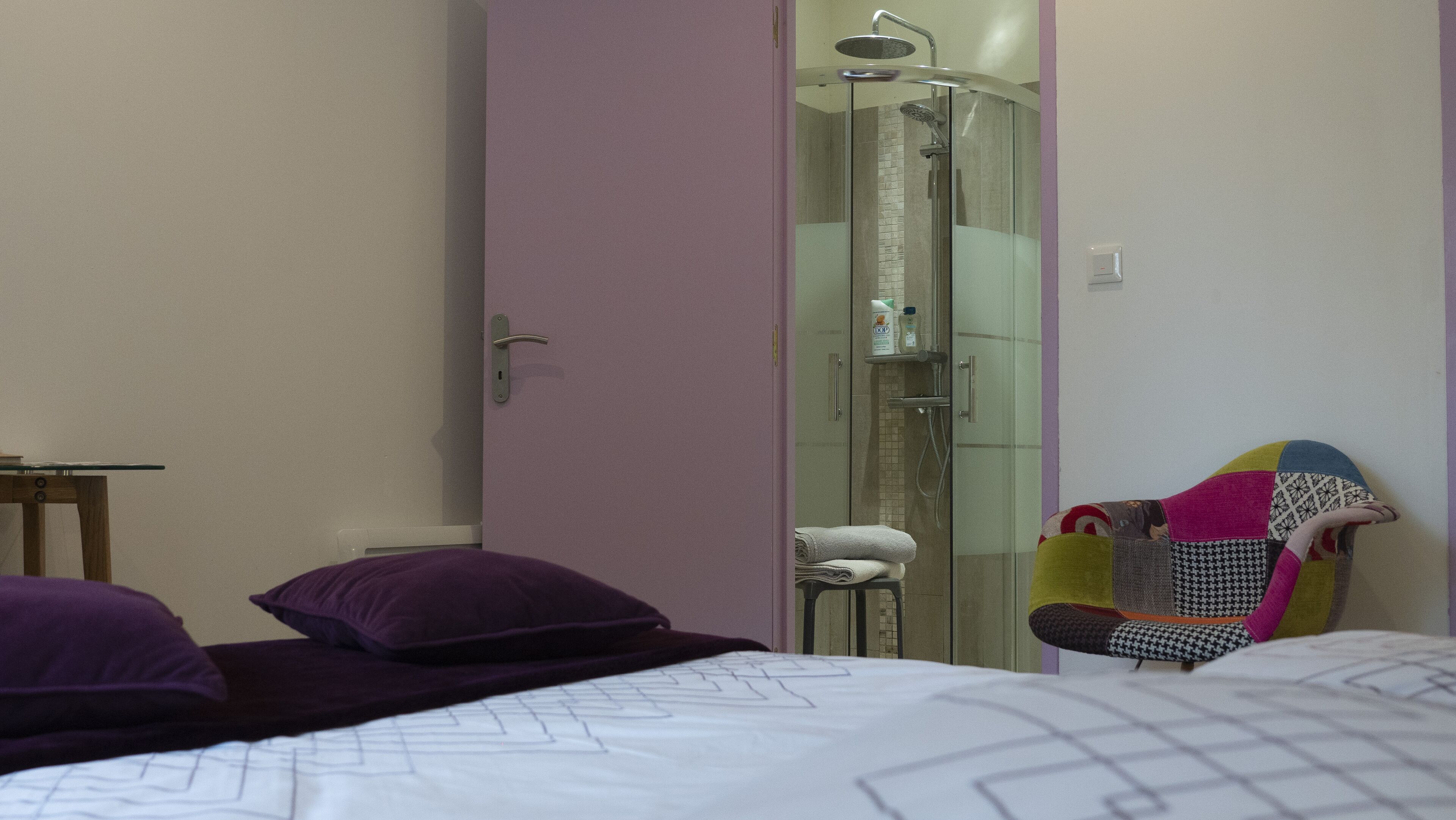 Une chambre à coucher avec un lit, des oreillers, une chaise et une douche fermée par des parois en verre.