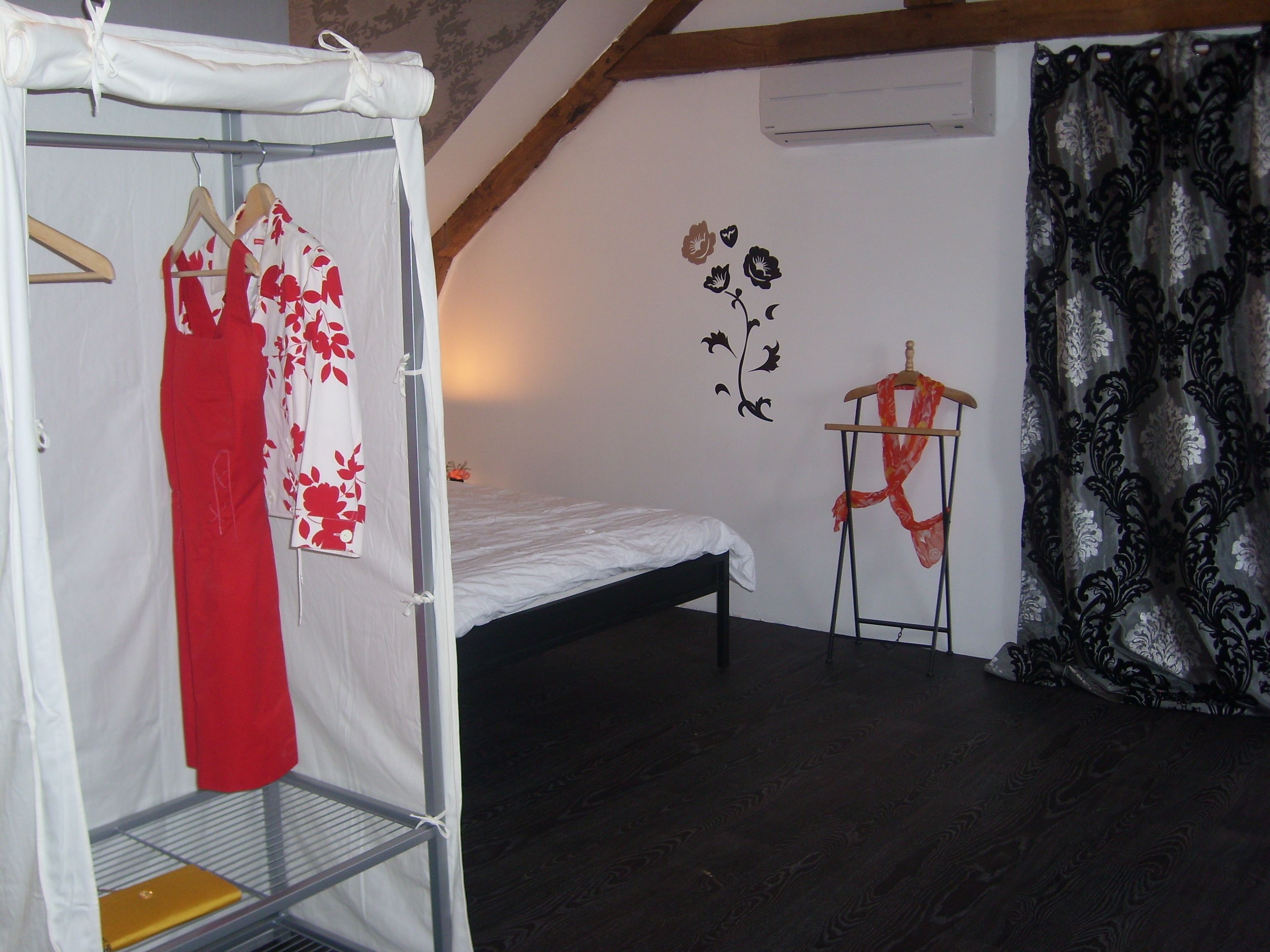 A bedroom with a single bed, a wardrobe, a drying rack, and a wall with floral decals.