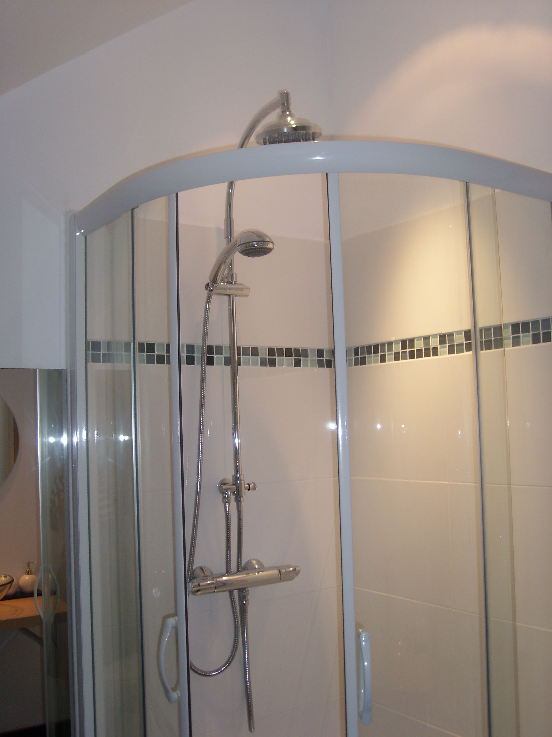 A glass-enclosed shower with a handheld showerhead and a fixed overhead showerhead.