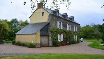 Traditional country house with a stone facade and attached structure, set amidst a well-mainters lawn.