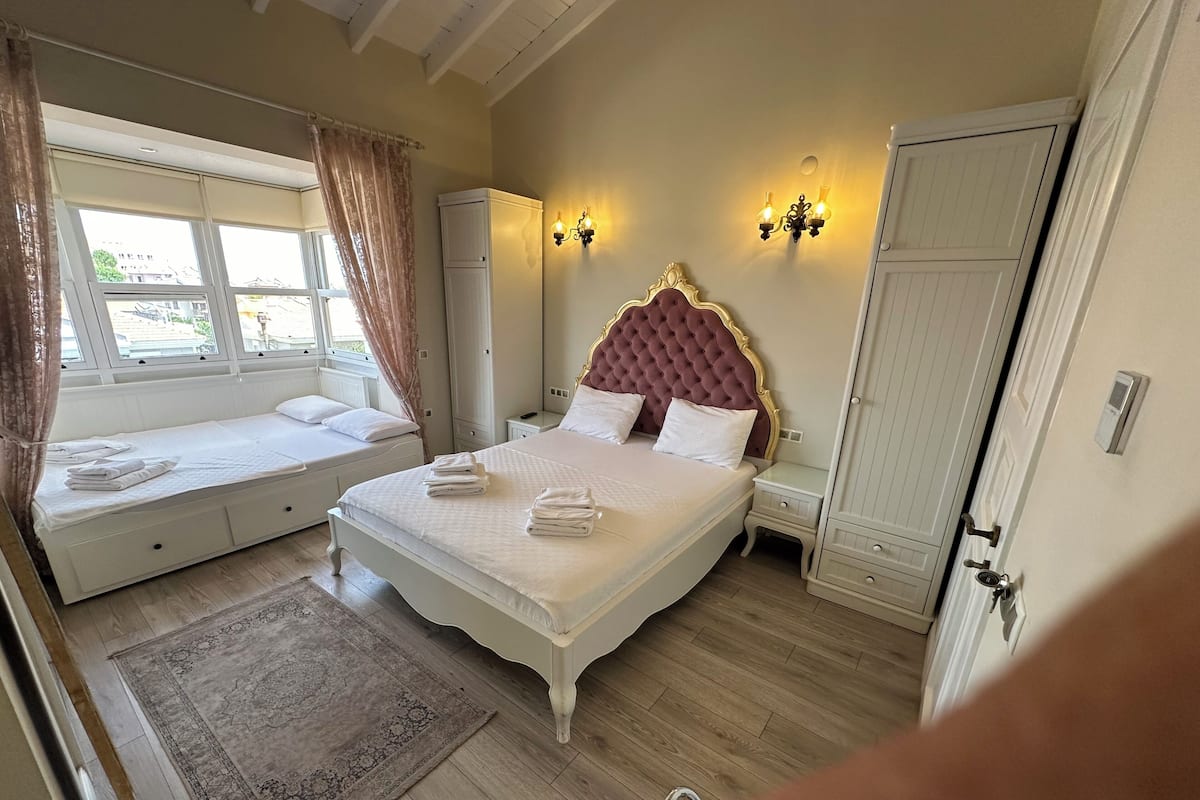 Ein Schlafzimmer mit einem großen Bett, einem kleineren Bett, einem Kleiderschrank, einem Nachttisch und einem Fenster mit Vorhängen.