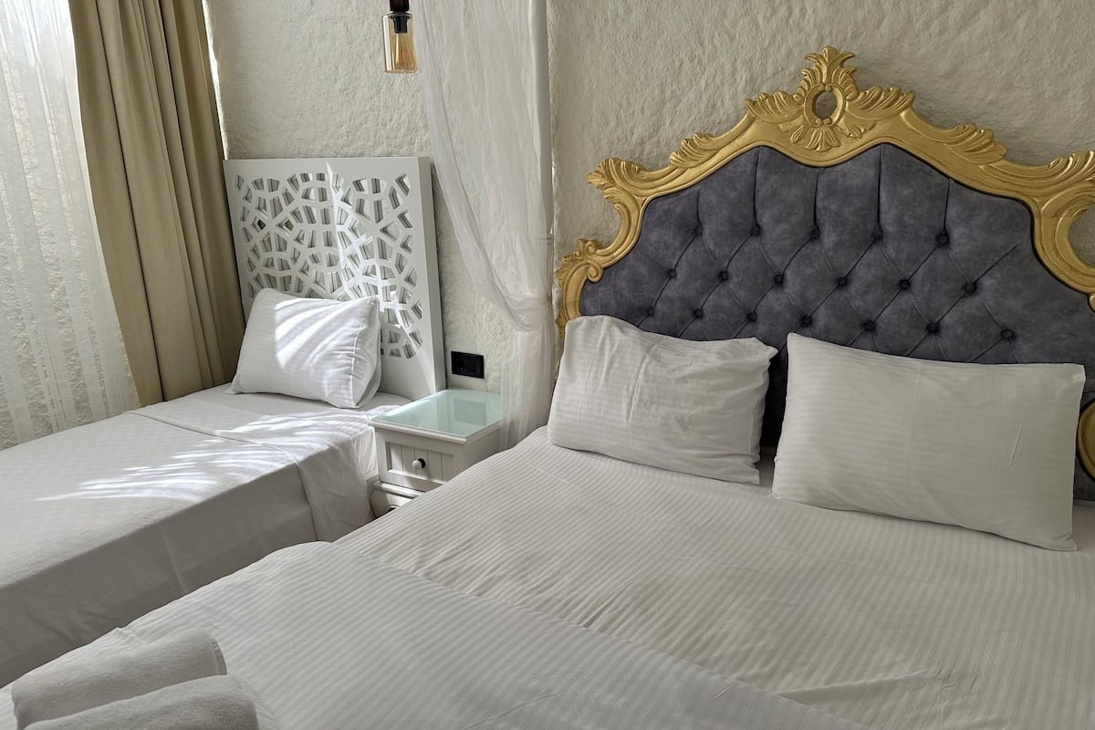 Ein Hotelzimmer mit zwei Betten, jeweils mit weißen Laken und Kissen, einem Nachttisch mit Lampe und einem dekorativen Kopfteil.