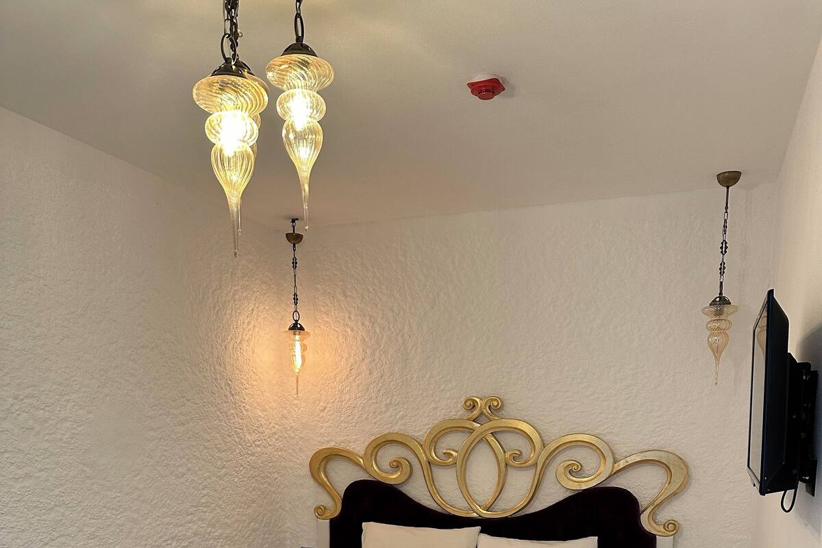 Ein ordentlich gemachtes Bett mit weißen Leinen, einem verzierten, goldenen Kopfteil und Nachttischen.