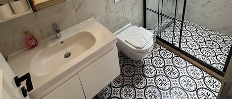 Un baño con lavamanos, inodoro y zona de ducha de mármol.