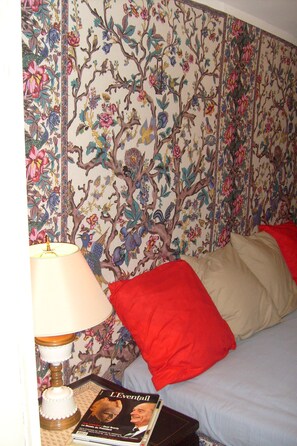 A bedroom with floral wallpaper, a red pillow, a lamp, and a magazine on the nightstand. - Château De Serrigny (Ladoix-Serrigny)