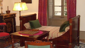 Une pièce avec un lit en bois, un bureau, une chaise, un lustre et une fenêtre avec des rideaux.