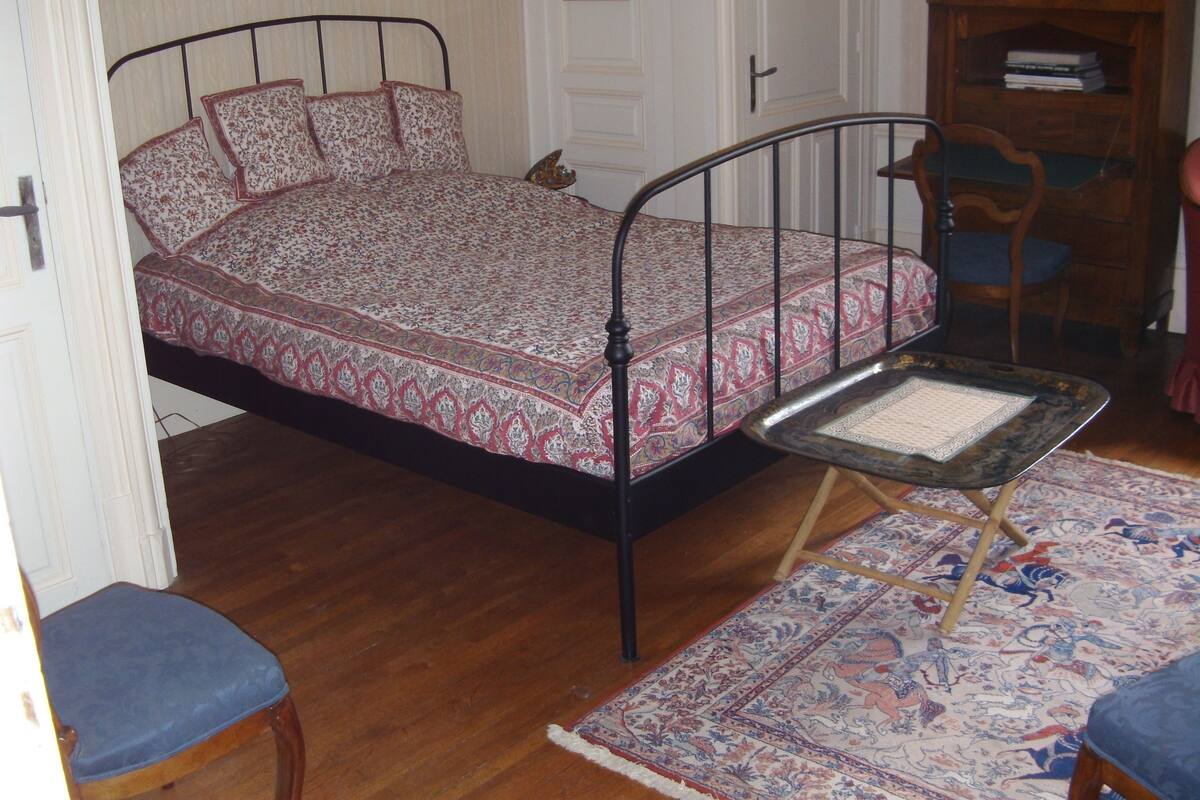 Un dormitorio con una cama, una mesita, una silla y una alfombra.