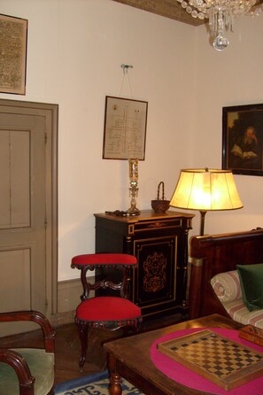 A room with a wooden chair, a small table with a chessboard, a lamp, and a framed picture on the wall. - Château De Serrigny (Ladoix-Serrigny)