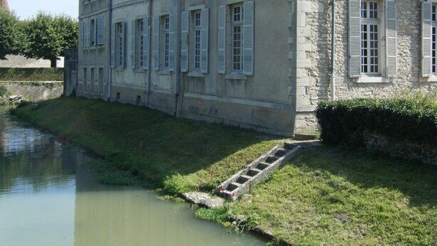 Un grand bâtiment en pierre, doté de nombreuses fenêtres et bordé d’un cours d’eau.