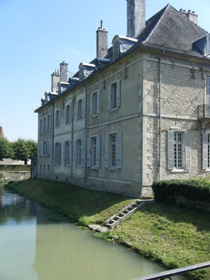 A large stone building with multiple windows and a waterway in front. - Château De Serrigny (Ladoix-Serrigny)