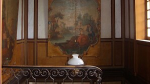 Une pièce ornée d’une grande fresque murale, d’un plafond agrémenté d’un luminaire décoratif et d’un escalier doté de rampes ouvragées.