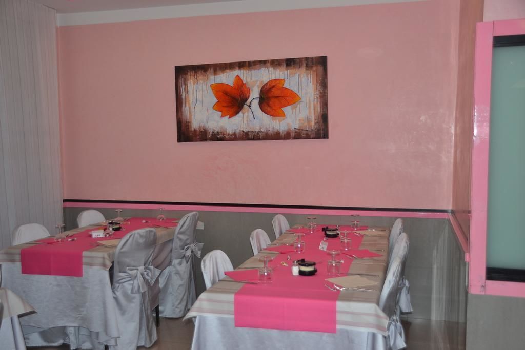 Un salón de conferencias con una larga mesa lista para una reunión, sillas con fundas blancas y un cuadro grande de hojas en la pared.