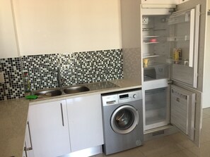 Eine kleine Küche mit Waschmaschine, Spüle und Kühlschrank.
