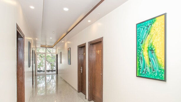 A hallway with wooden doors, a large abstract painting on the wall, and a polished floor. - OYO 490 Hotel Compact Maple Leaf (Bengaluru)