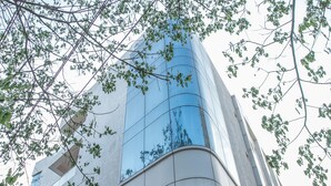 A modern building with a curved facade, large windows, and a red structural element at the base. - OYO 490 Hotel Compact Maple Leaf (Bengaluru)