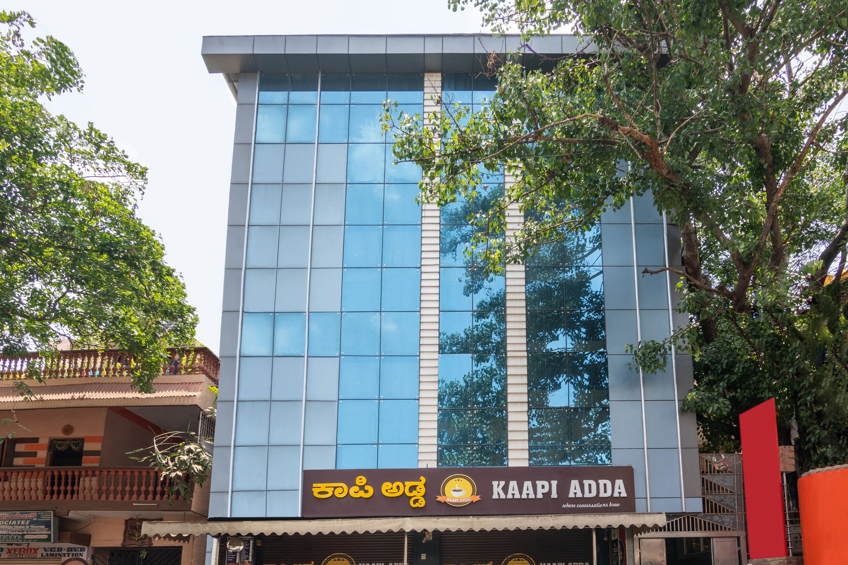 A modern building with a reflective glass facade and a sign for "Kaapi Adda" restaurant.