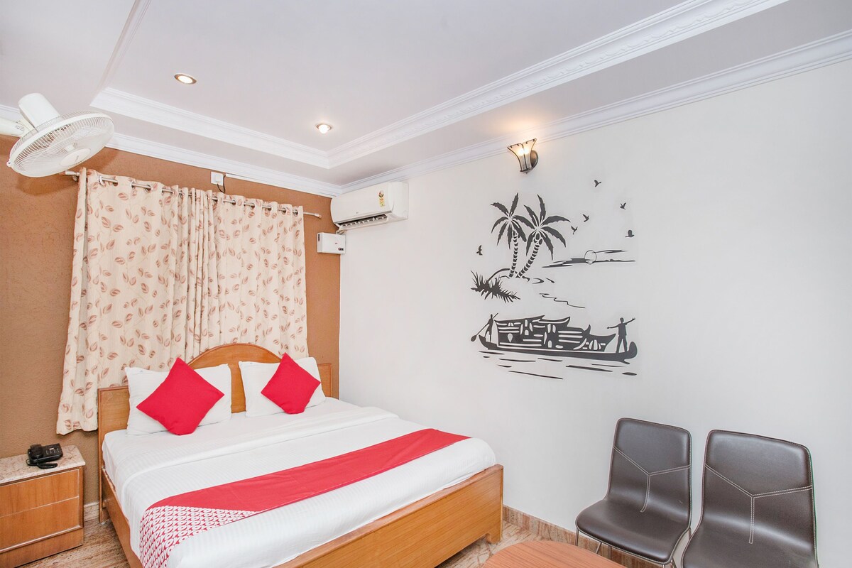 A hotel room with a bed, a desk, a chair, a fan, and a wall with a tropical mural.