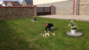 Criança brincando com blocos de madeira numerados em um gramado com um muro de pedra e um prédio ao fundo.