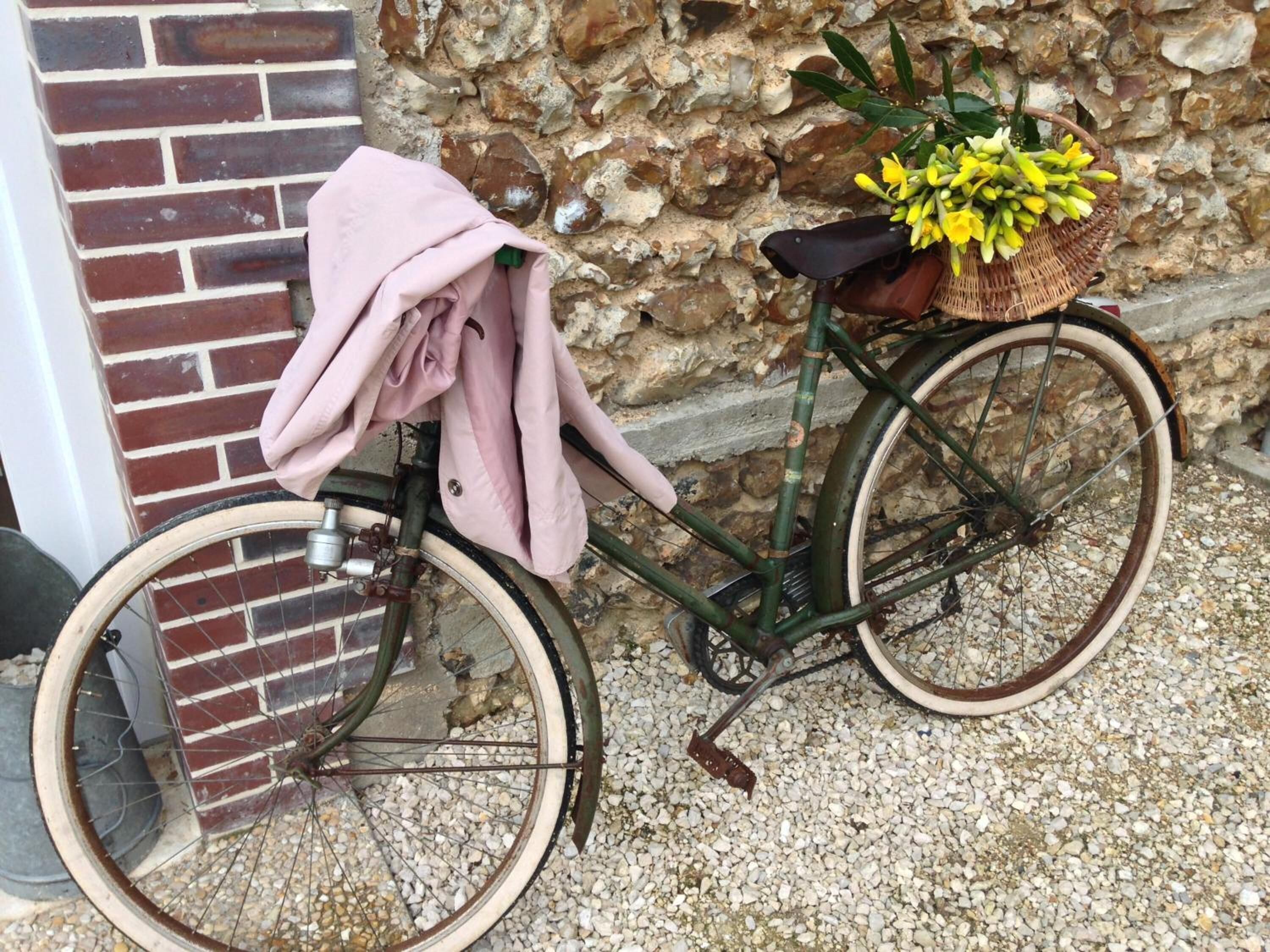 A bicycle with a basket and a pink cloth, parked against a stone wall.