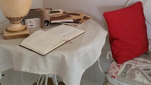 A room with a table, a lamp, a chair, a red pillow, and framed pictures on the wall. - La Ferme du Bois Paris (Ermenonville-la-Petite)