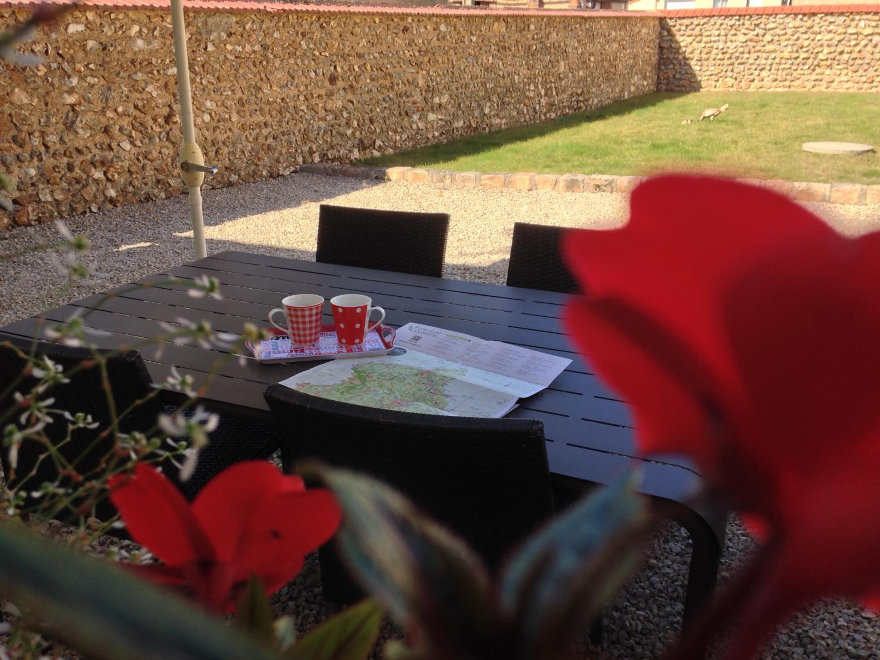 A table with a map and two mugs, set against a stone wall and a grassy area.