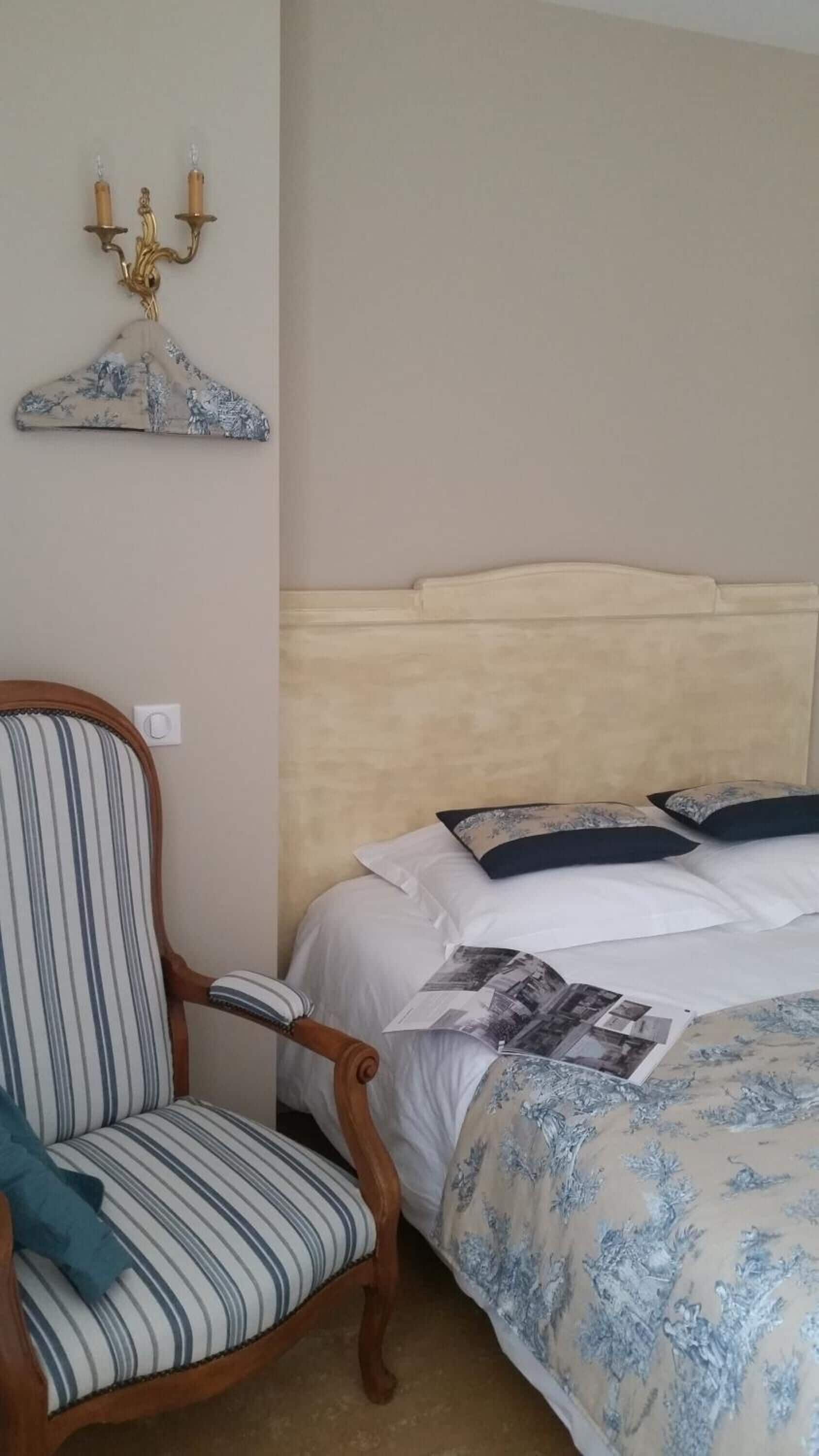 Un dormitorio con cama, una silla y un candelabro fijado a la pared.