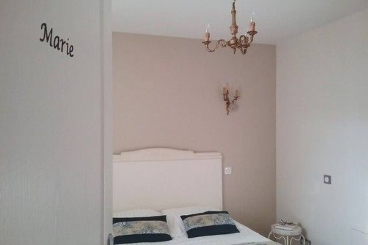 A bedroom with a bed, a chandelier, and a wall-mounted light fixture.