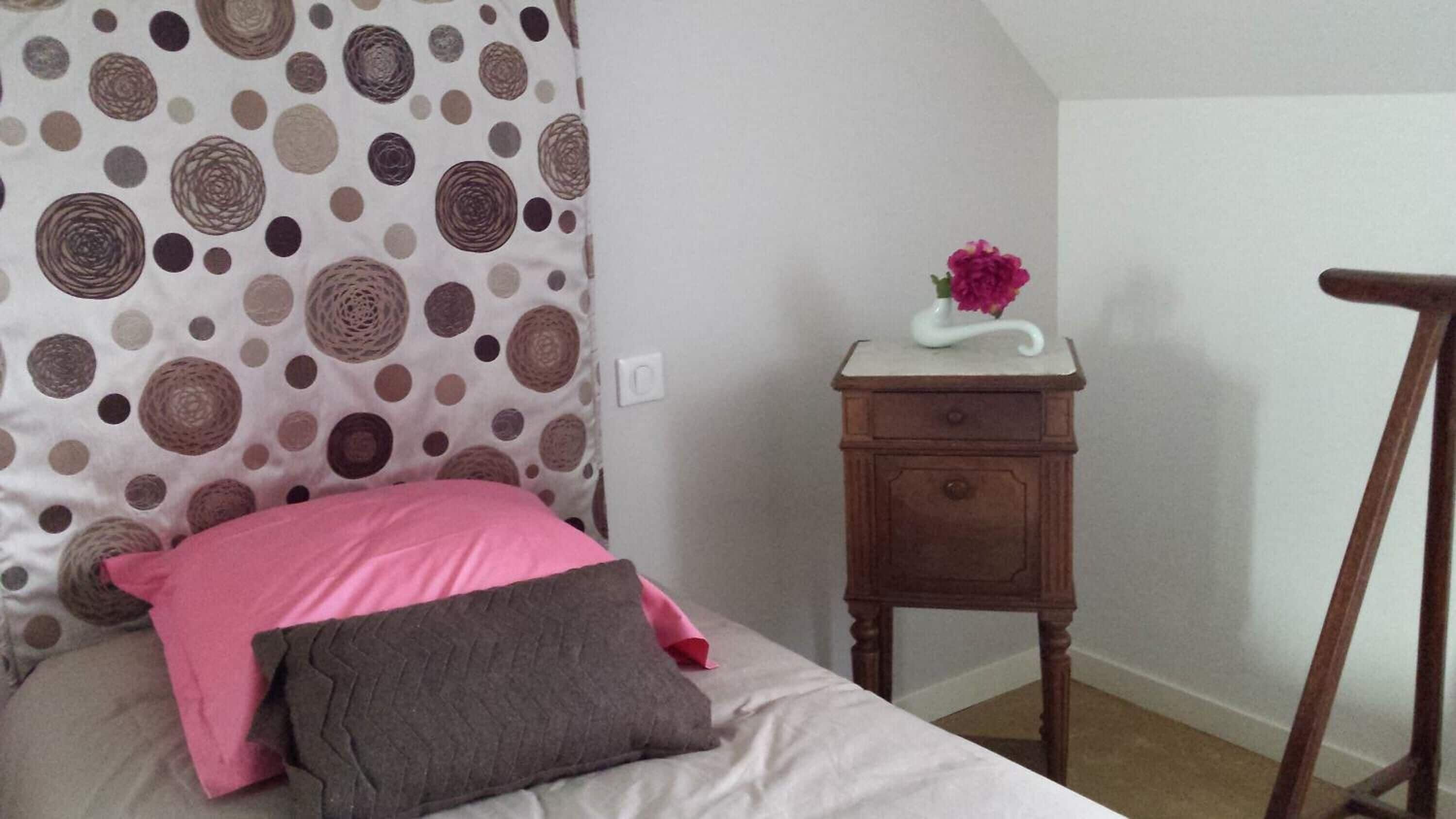 Un dormitorio con cama, una mesita de noche con un florero y una silla de madera.