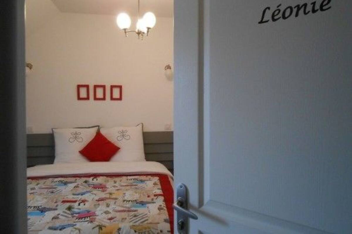 A bedroom with a bed, a chandelier, and a door with the name 'Léonie' on it.