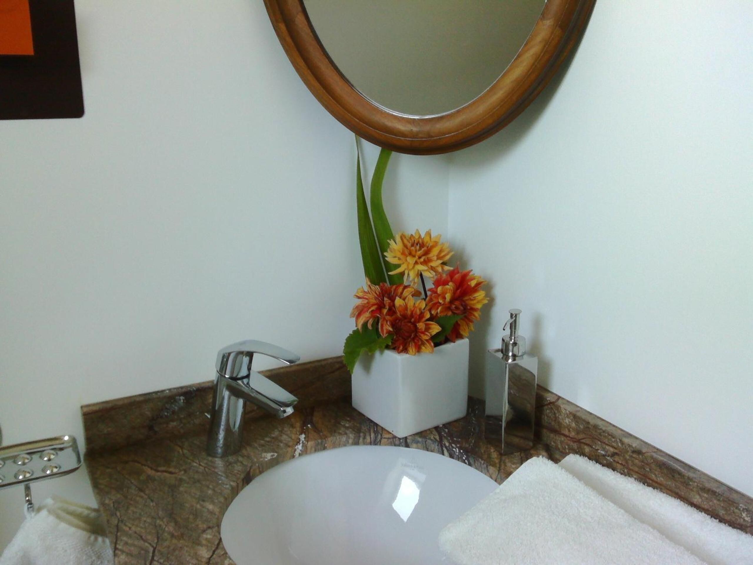 Une salle de bain avec un lavabo blanc, un miroir, un robinet et un vase à fleurs.