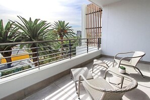 A balcony with wicker furniture, a potted plant, and a view of palm trees and buildings.