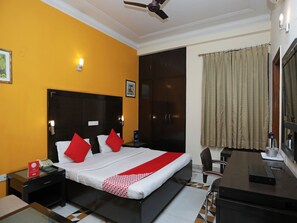 A hotel room with a bed, a desk, a chair, a telephone, and a ceiling fan. - OYO 12075 Hotel Regalia Retreat (New Delhi)