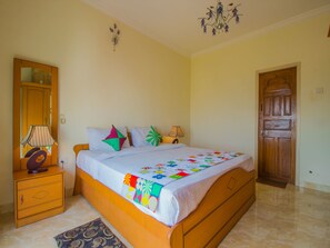 A bedroom with a bed, a nightstand, a lamp, a mirror, and a door. - OYO 12867 Home Luxurious 2BHK Near Airport (Vasco da Gama)