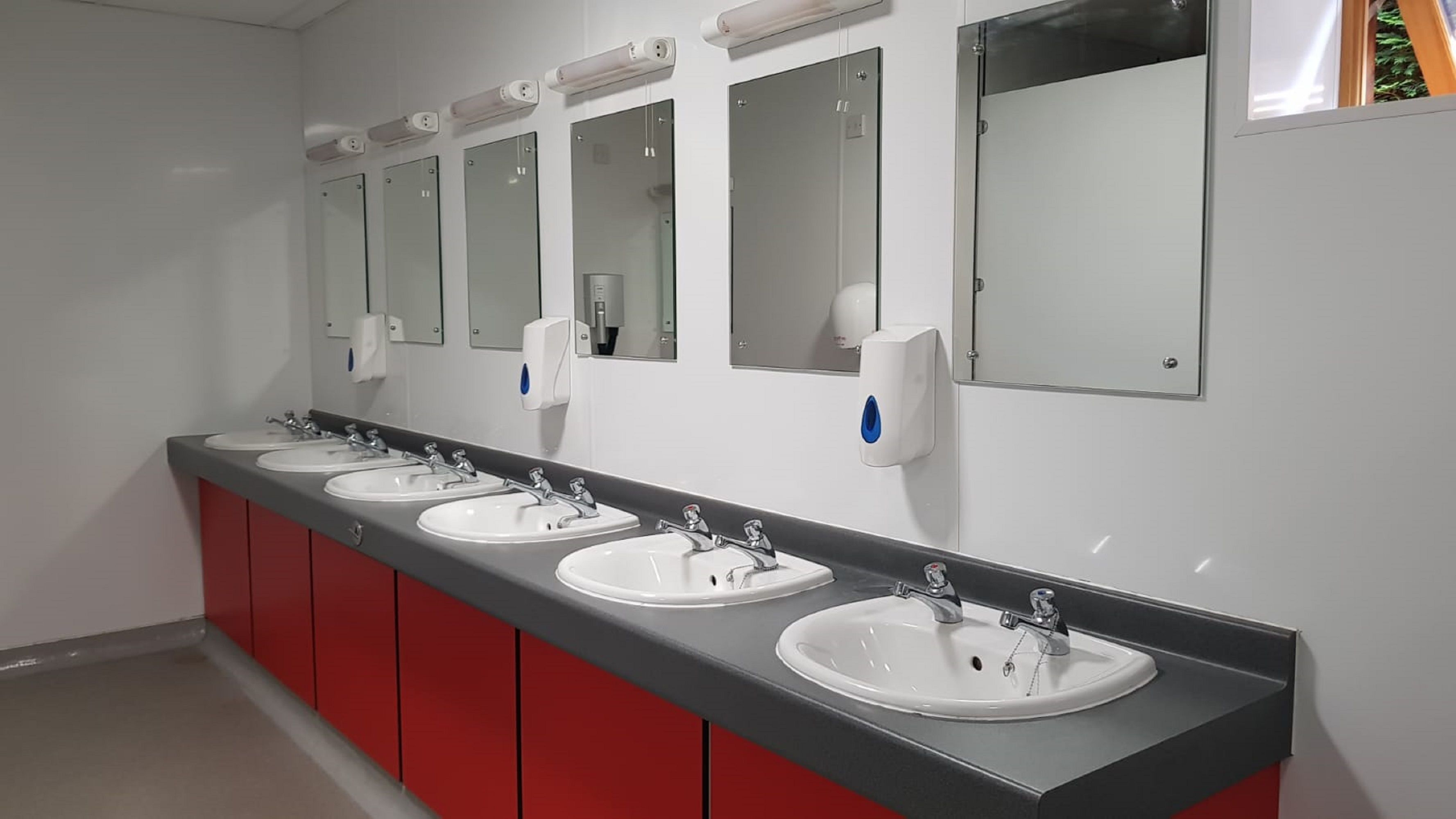 A row of sinks with mirrors and soap dispensers in a restroom.