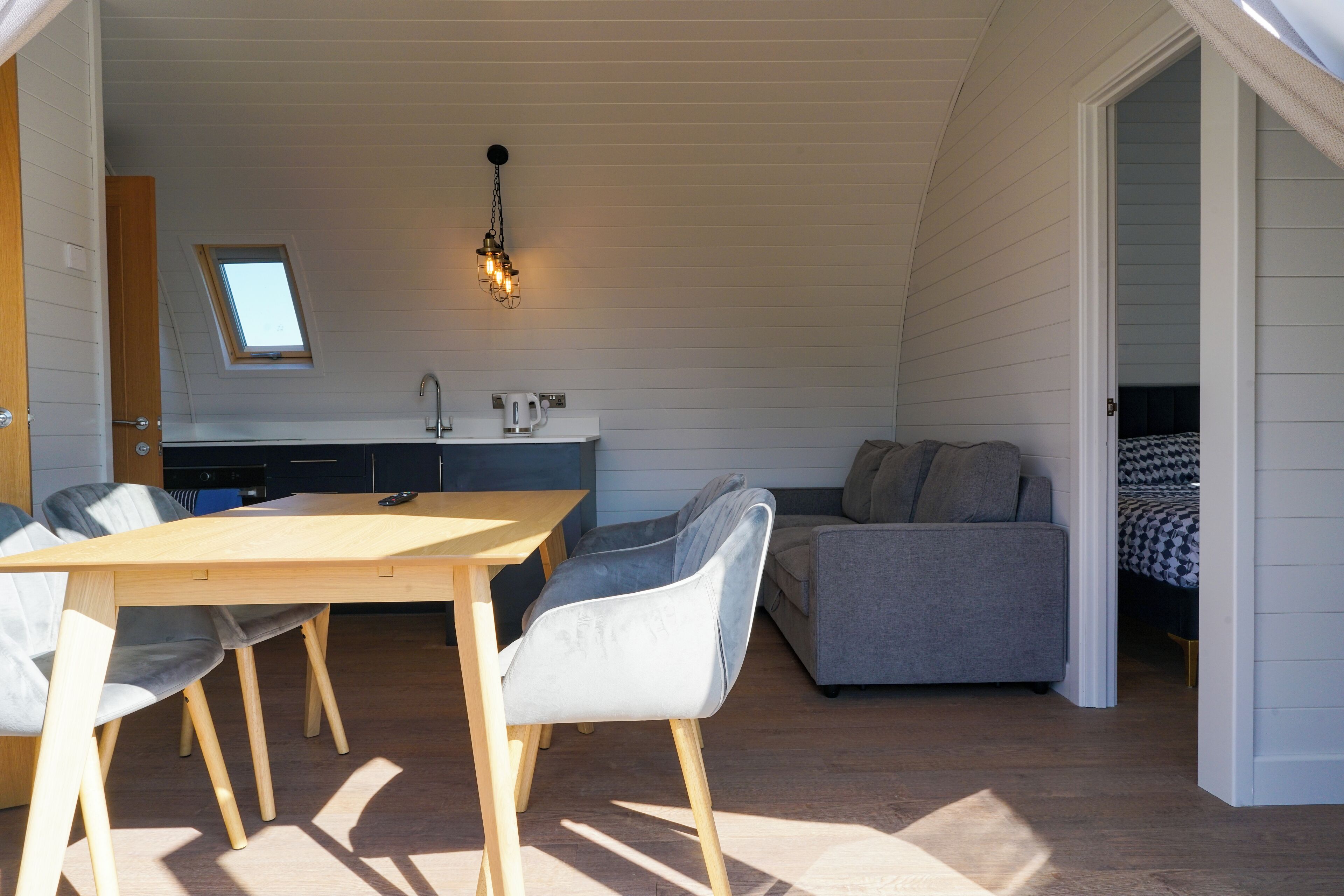 A compact, well-lit room with a dining table, chairs, a sofa, and a kitchenette.