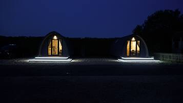 Two dome-shaped cabins with illuminated entryways, set on a gravel path at dusk.