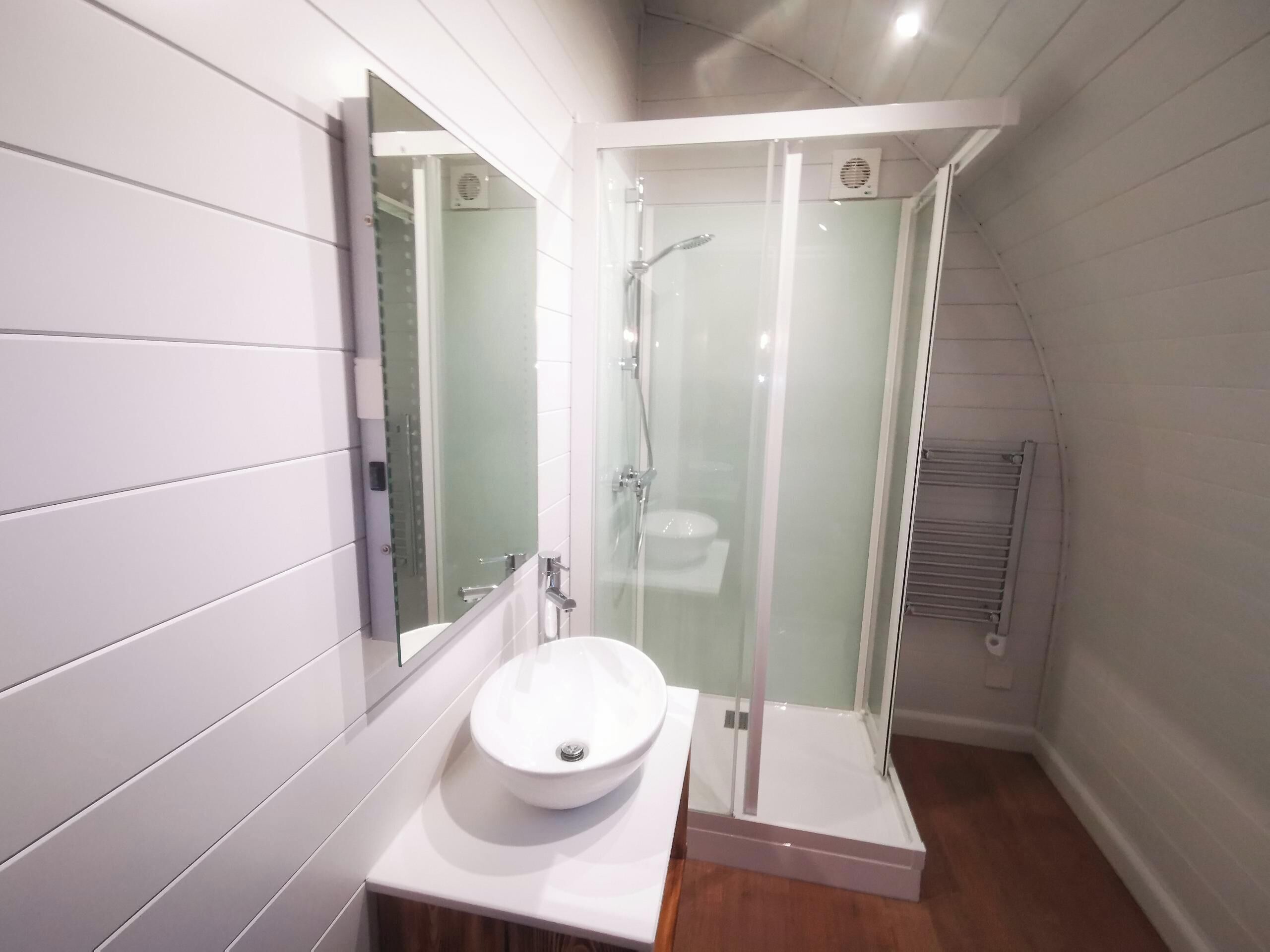 Un bagno moderno con un lavandino bianco, una cabina doccia in vetro e uno specchio sopra il lavandino.