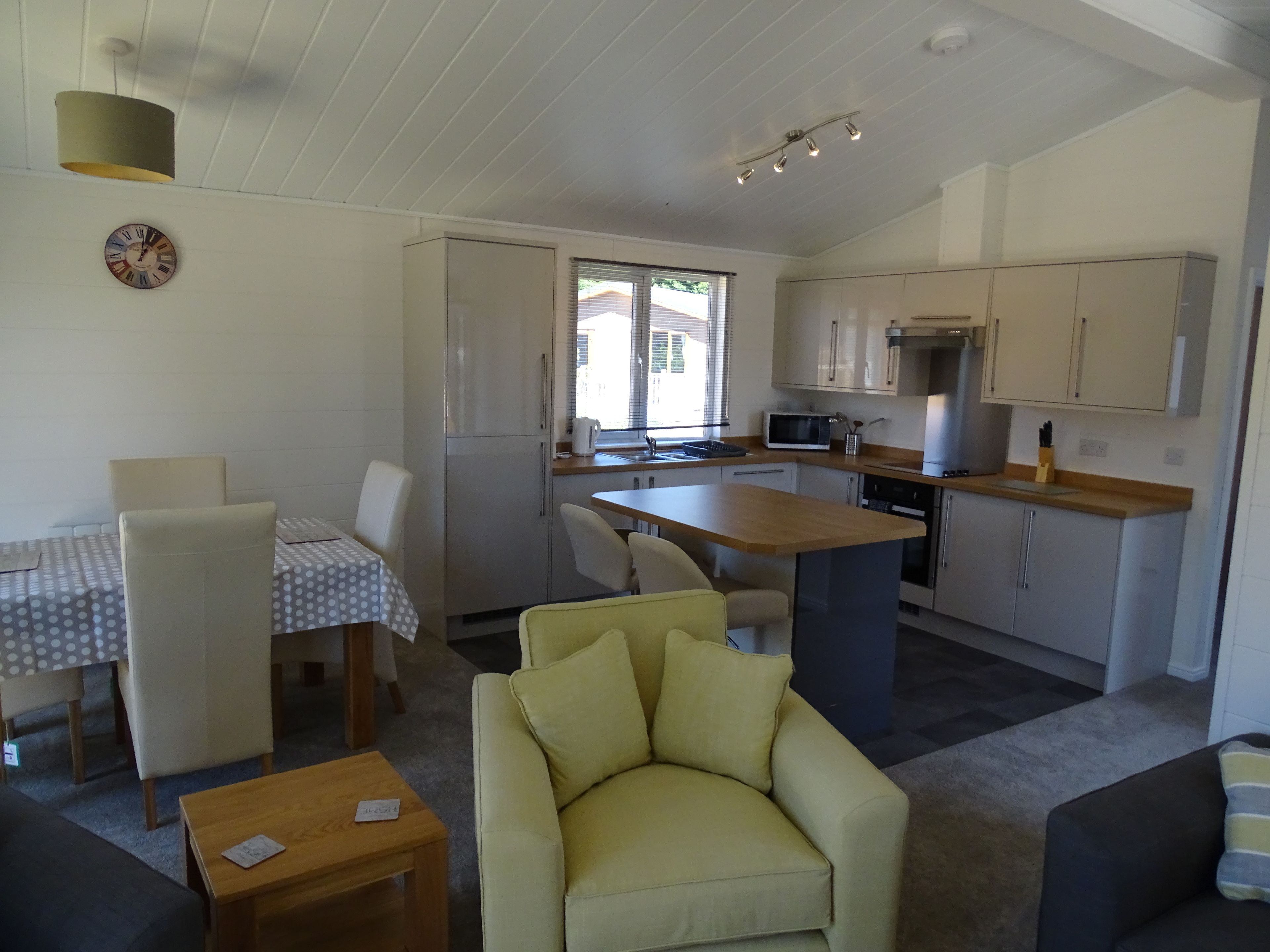 A compact living space with a dining area, a sofa, a kitchen with a microwave, and a clock on the wall.