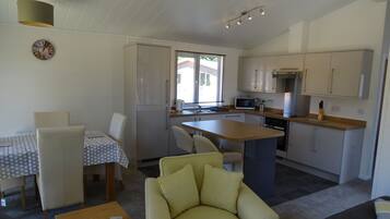 A compact living space with a dining area, a sofa, a kitchen with a microwave, and a clock on the wall.