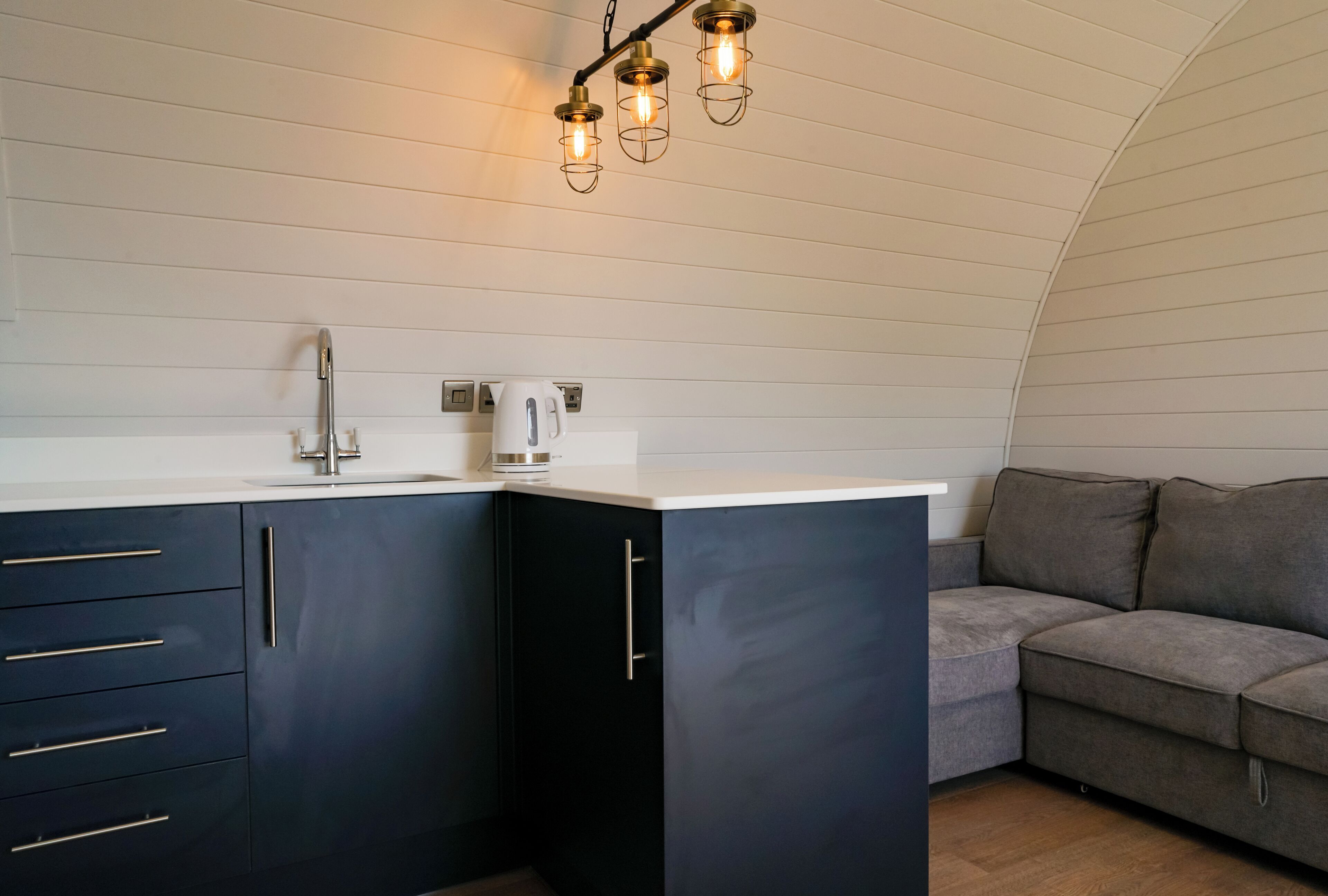 A compact kitchen with dark cabinets, a white countertop, a kettle, and a modern faucet.