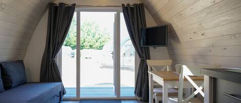 A cozy room with a wooden ceiling, a sofa, a table, a chair, and a TV mounted on the wall.