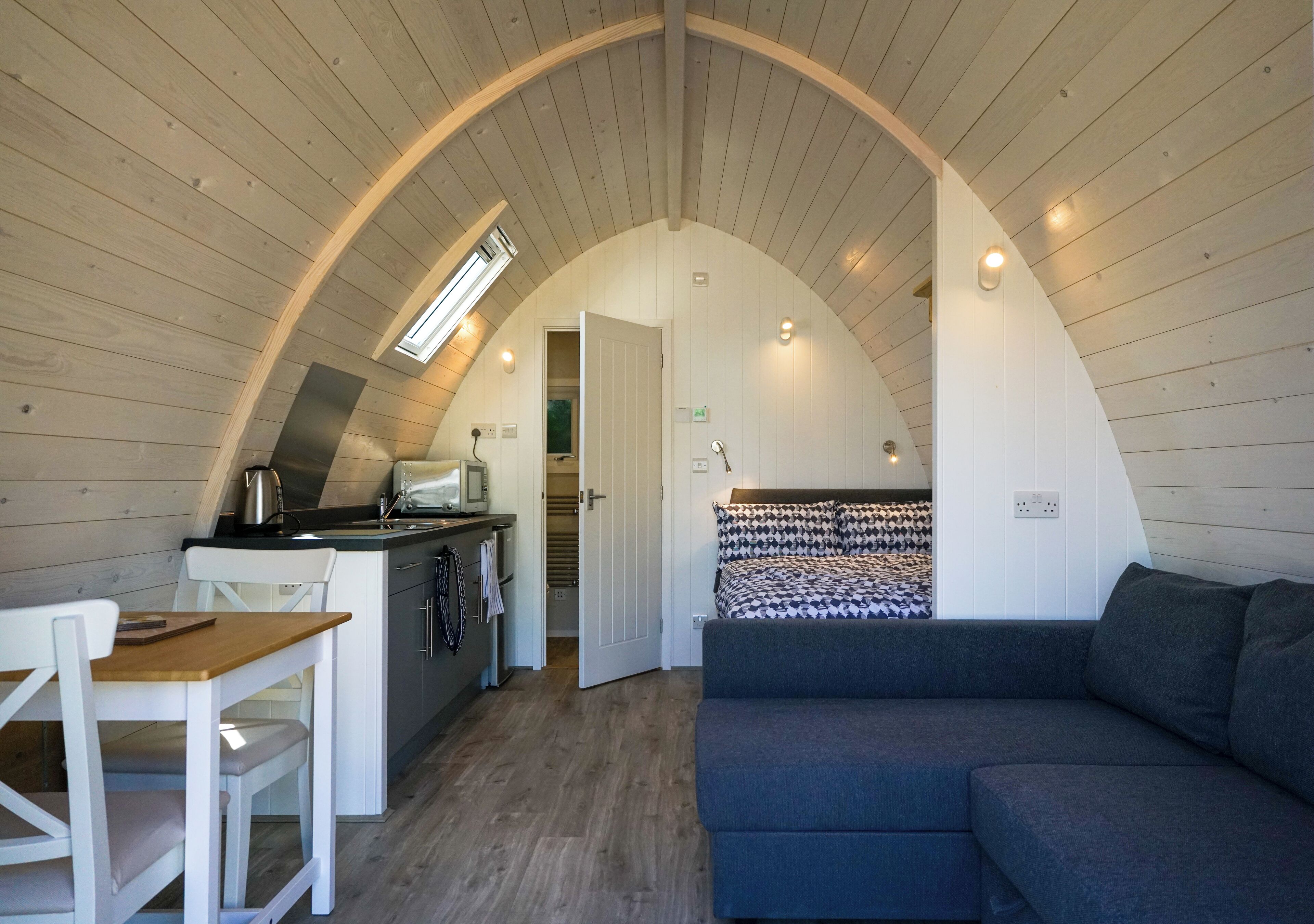 A cozy loft-style room with a curved ceiling, a kitchenette, a dining area, and a large bed.