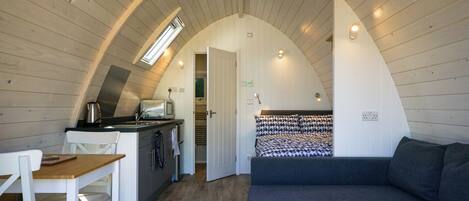 A cozy loft-style room with a curved ceiling, a kitchenette, a dining area, and a large bed.
