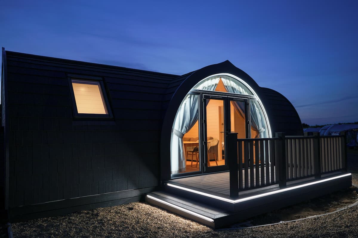 Un bâtiment moderne aux couleurs sombres, doté d’une grande porte en verre en arc de cercle qui donne accès à un espace intérieur.